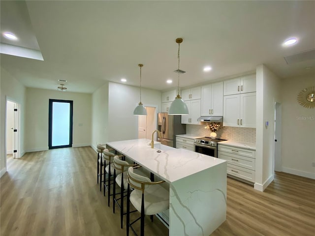 3616 Bellefonte Ave, North Port, FL 34286 - kitchen with stainless steel appliances, decorative backsplash, an island with sink, light wood finished floors, and under cabinet range hood