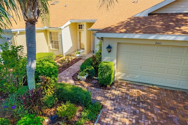 2411 New Haven Cir Unit 70, Sun City Center, FL 33573 - property entrance featuring roof with shingles, an attached garage, stucco siding, and decorative driveway