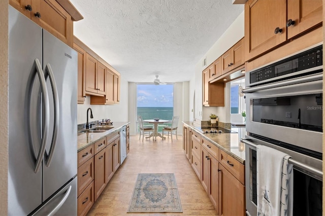 2425 Gulf Of Mexico Dr Unit 10F, Longboat Key, FL 34228 - kitchen with stainless steel appliances, a textured ceiling, light stone countertops, light wood-style flooring, and brown cabinetry