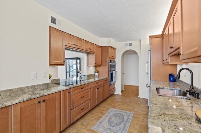 2425 Gulf Of Mexico Dr Unit 10F, Longboat Key, FL 34228 - kitchen featuring arched walkways, appliances with stainless steel finishes, a textured ceiling, light stone countertops, and brown cabinetry