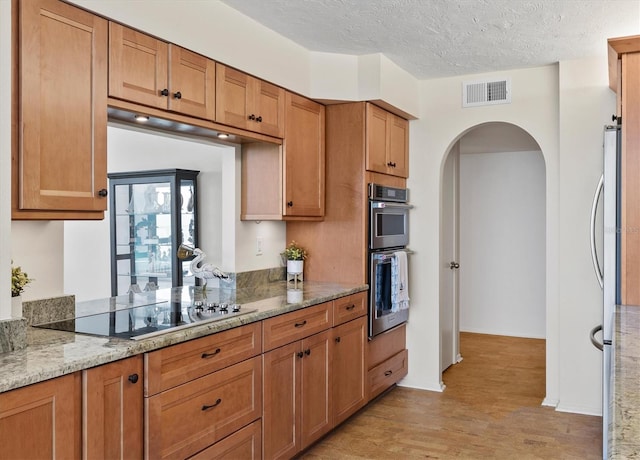 2425 Gulf Of Mexico Dr Unit 10F, Longboat Key, FL 34228 - kitchen featuring appliances with stainless steel finishes, arched walkways, light wood-type flooring, a textured ceiling, and light stone countertops