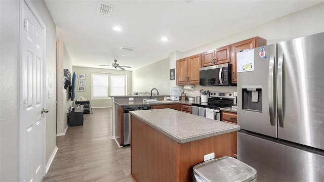 8907 White Sage Loop, Lakewood Ranch, FL 34202 - kitchen featuring appliances with stainless steel finishes, a peninsula, brown cabinetry, light wood-type flooring, and a kitchen island