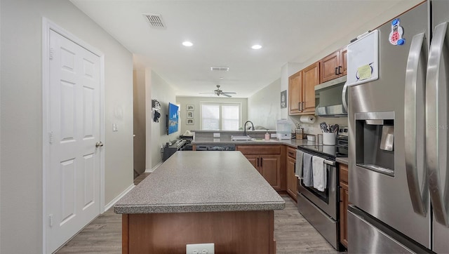8907 White Sage Loop, Lakewood Ranch, FL 34202 - kitchen with appliances with stainless steel finishes, light wood-style floors, a center island, brown cabinetry, and recessed lighting