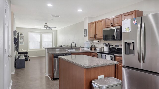 8907 White Sage Loop, Lakewood Ranch, FL 34202 - kitchen with appliances with stainless steel finishes, a peninsula, brown cabinetry, a kitchen island, and a ceiling fan