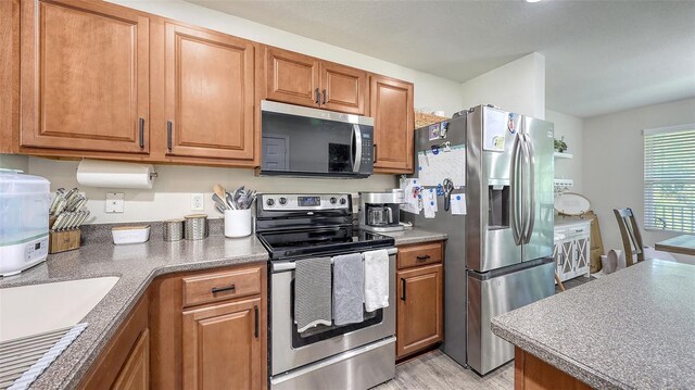 8907 White Sage Loop, Lakewood Ranch, FL 34202 - kitchen with appliances with stainless steel finishes, brown cabinetry, and light wood finished floors