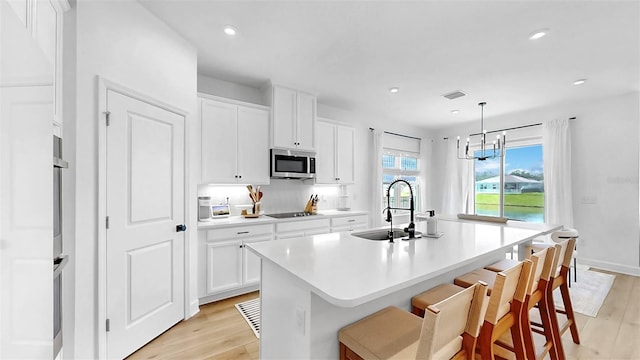 6120 115th Ave E, Parrish, FL 34219 - kitchen with stainless steel microwave, black electric cooktop, light wood-type flooring, an island with sink, and light countertops