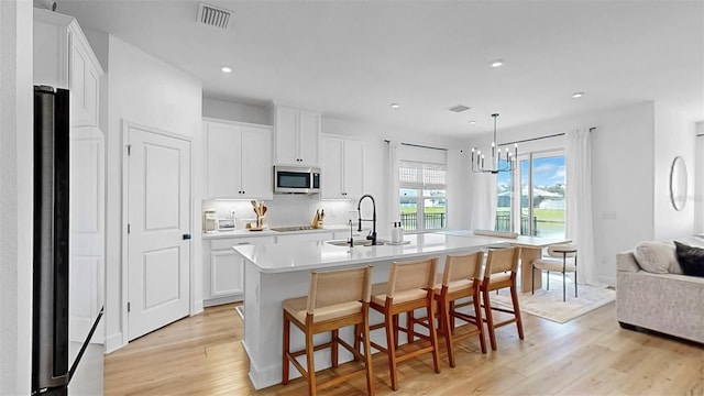 6120 115th Ave E, Parrish, FL 34219 - kitchen featuring stainless steel microwave, light wood-type flooring, light countertops, an island with sink, and white cabinets