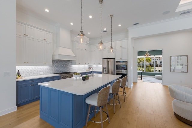 16511 Cornwall Ln, Lakewood Ranch, FL 34202 - kitchen featuring appliances with stainless steel finishes, blue cabinets, custom range hood, light wood-style flooring, and decorative backsplash