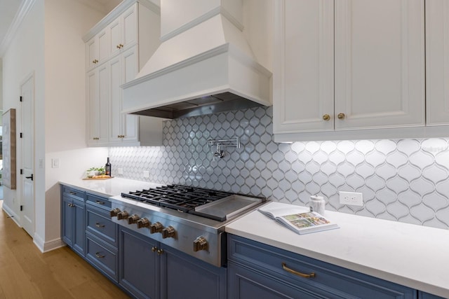 16511 Cornwall Ln, Lakewood Ranch, FL 34202 - kitchen with blue cabinetry, custom exhaust hood, white cabinetry, light wood-style flooring, and light countertops