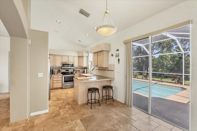 815 Greenview Dr, Apollo Beach, FL 33572 - kitchen with stainless steel appliances, stone tile floors, light brown cabinets, lofted ceiling, and a kitchen breakfast bar
