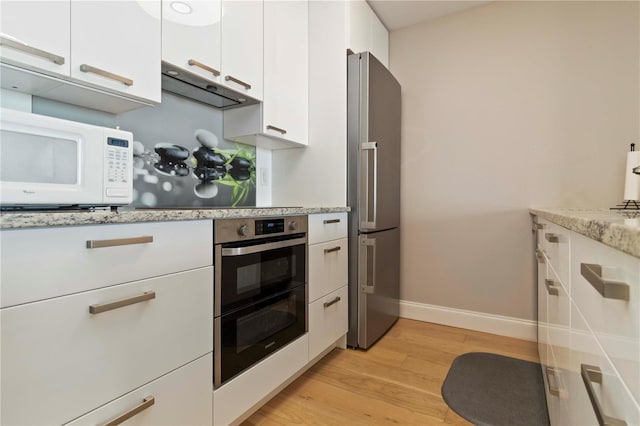 750 N Tamiami Trl Unit 1005, Sarasota, FL 34236 - kitchen with stainless steel appliances, light wood-style floors, white cabinetry, under cabinet range hood, and light stone counters