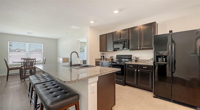 3813 Willow Branch Pl, Palmetto, FL 34221 - kitchen with black appliances, a breakfast bar, a kitchen island with sink, light stone counters, and recessed lighting