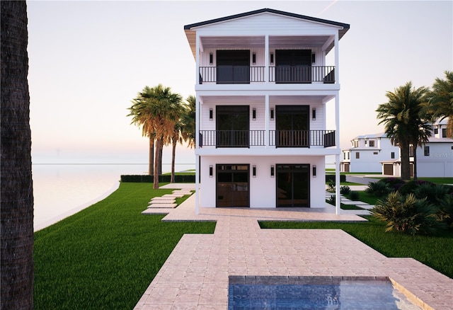 312 Avenida Leona, Sarasota, FL 34242 - back of property at dusk featuring a balcony, a lawn, a water view, a patio area, and stucco siding
