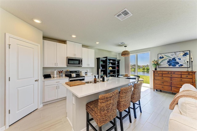 7160 Amelia River Dr, Parrish, FL 34219 - kitchen featuring appliances with stainless steel finishes, light countertops, white cabinetry, a kitchen breakfast bar, and a kitchen island with sink