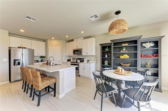 7160 Amelia River Dr, Parrish, FL 34219 - kitchen featuring appliances with stainless steel finishes, a kitchen island with sink, a breakfast bar area, white cabinets, and light countertops