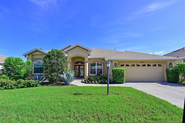 10571 Old Grove Cir, Bradenton, FL 34212 - view of front facade featuring stucco siding, an attached garage, a front lawn, driveway, and french doors