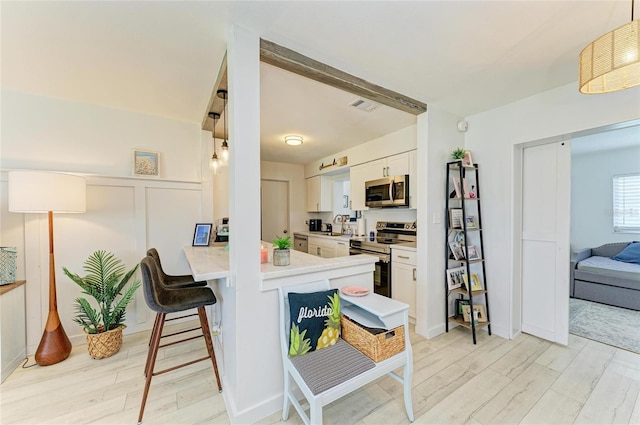 237 Saxon Cir, Venice, FL 34293 - kitchen featuring appliances with stainless steel finishes, light countertops, white cabinetry, a breakfast bar, and light wood-style floors