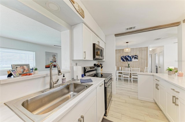 237 Saxon Cir, Venice, FL 34293 - kitchen featuring appliances with stainless steel finishes, white cabinets, light wood-style flooring, light countertops, and decorative light fixtures