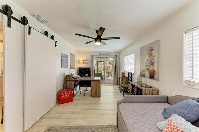 237 Saxon Cir, Venice, FL 34293 - bedroom featuring a barn door, a desk, light wood-style floors, a textured ceiling, and a ceiling fan