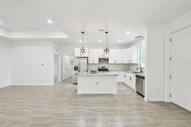 2523 Hagerick Ln, North Port, FL 34288 - kitchen featuring appliances with stainless steel finishes, a kitchen island, white cabinetry, decorative backsplash, and light stone counters