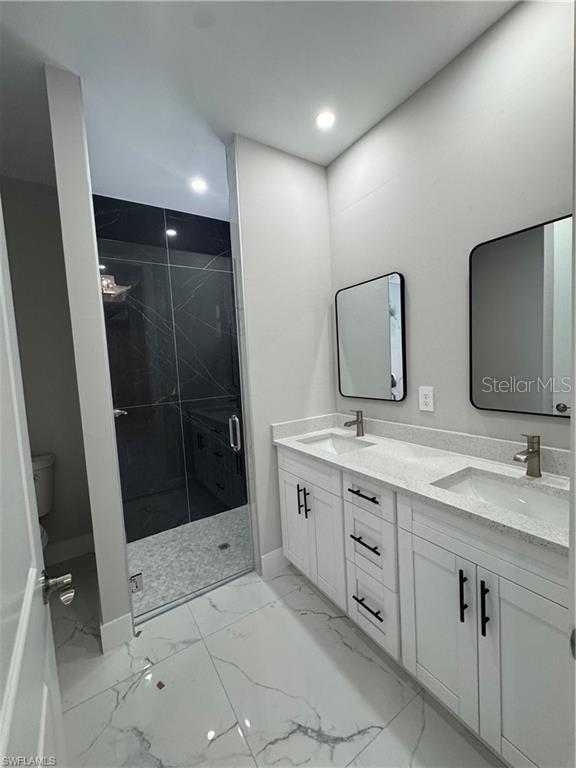 3003 18th St W, Lehigh Acres, FL 33971 - bathroom with double vanity, a marble finish shower, marble finish flooring, and recessed lighting
