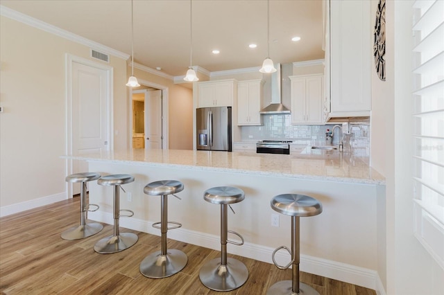 501 Tamiami Trl N Unit 201, Venice, FL 34285 - kitchen with appliances with stainless steel finishes, wall chimney range hood, white cabinets, light stone countertops, and a peninsula