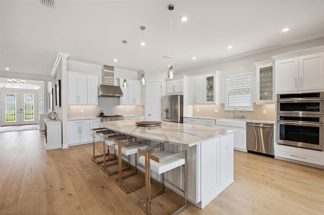 3968 Santa Caterina Blvd, Bradenton, FL 34211 - kitchen featuring appliances with stainless steel finishes, wall chimney exhaust hood, a kitchen island, ornamental molding, and a breakfast bar