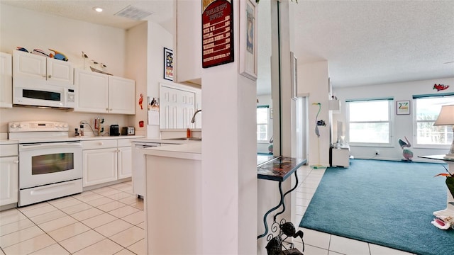 5078 47th St W, Bradenton, FL 34210 - kitchen with white appliances, a textured ceiling, white cabinetry, light tile patterned floors, and light carpet