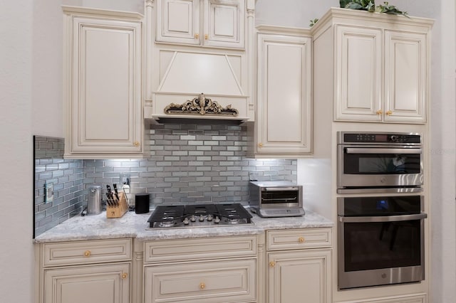 5804 Mulligan Way, Lakewood Ranch, FL 34211 - kitchen featuring appliances with stainless steel finishes, cream cabinets, decorative backsplash, premium range hood, and light stone countertops