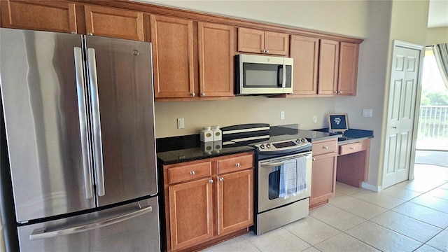 1251 Burgos Dr Unit 303, Sarasota, FL 34238 - kitchen featuring appliances with stainless steel finishes, light tile patterned floors, brown cabinets, and dark stone countertops