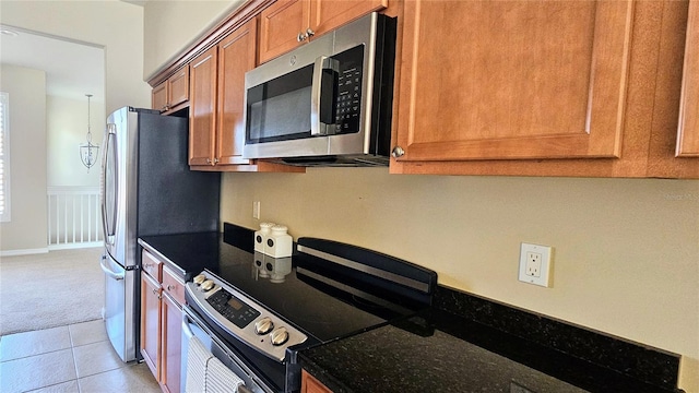 1251 Burgos Dr Unit 303, Sarasota, FL 34238 - kitchen with appliances with stainless steel finishes, brown cabinets, light carpet, light tile patterned floors, and dark stone counters