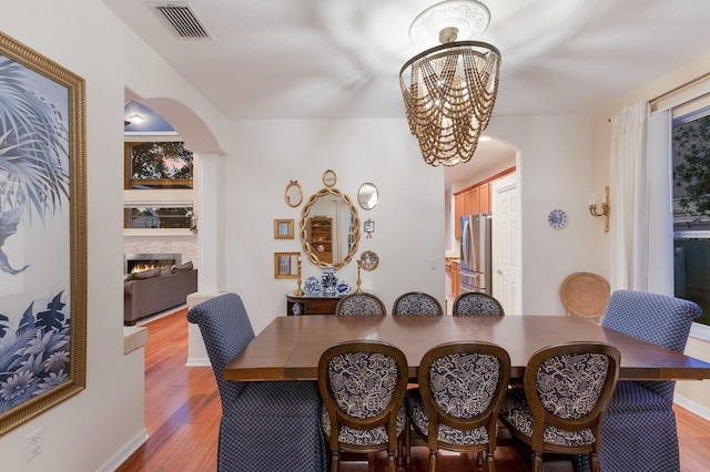 4410 67th Avenue Cir E, Sarasota, FL 34243 - dining space featuring arched walkways, light wood finished floors, a chandelier, and a warm lit fireplace