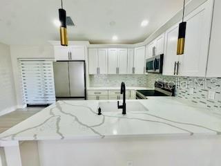 5009 Jody Ave, North Port, FL 34288 - kitchen featuring stainless steel appliances, backsplash, pendant lighting, white cabinetry, and a peninsula
