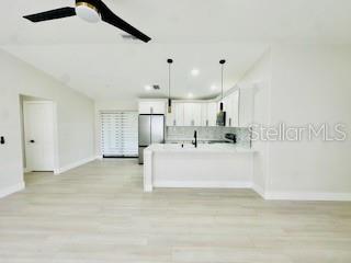 5009 Jody Ave, North Port, FL 34288 - kitchen featuring freestanding refrigerator, a peninsula, white cabinetry, light wood-style floors, and hanging light fixtures