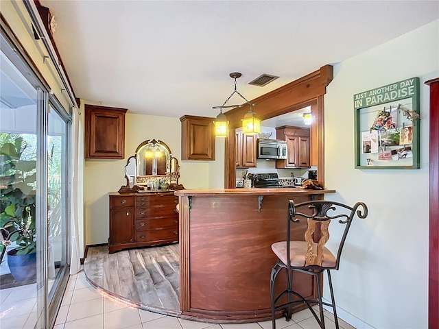 408 67th Ave W, Bradenton, FL 34207 - kitchen featuring stainless steel microwave, range, a kitchen bar, a peninsula, and hanging light fixtures