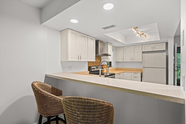 3003 Quail Holw Unit 10, Sarasota, FL 34235 - kitchen with freestanding refrigerator, wall chimney exhaust hood, stainless steel electric range, a tray ceiling, and a peninsula