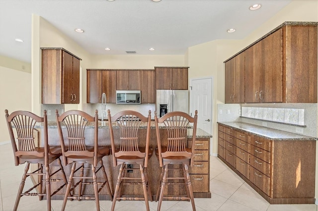 7005 Goldrush Ln, Bradenton, FL 34201 - kitchen featuring appliances with stainless steel finishes, light tile patterned floors, brown cabinetry, dark stone countertops, and recessed lighting