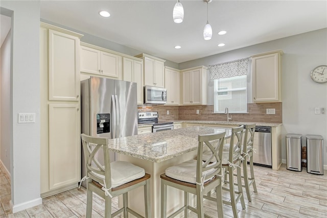 11625 Renaissance Blvd, Venice, FL 34293 - kitchen with stainless steel appliances, decorative backsplash, light stone countertops, a center island, and light wood-type flooring