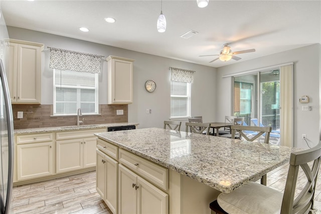 11625 Renaissance Blvd, Venice, FL 34293 - kitchen with a kitchen bar, decorative backsplash, a ceiling fan, a kitchen island, and light stone counters