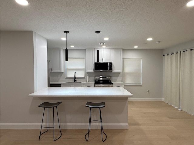 4661 Linwood St, Sarasota, FL 34232 - kitchen featuring stainless steel appliances, a textured ceiling, a breakfast bar area, light countertops, and light wood finished floors