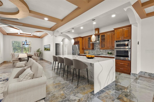 5714 38th Ave E, Bradenton, FL 34208 - kitchen with stainless steel appliances, arched walkways, brown cabinetry, backsplash, and a large island