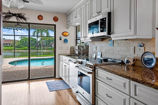 8703 53rd Ave W, Bradenton, FL 34210 - kitchen featuring appliances with stainless steel finishes, light wood-style floors, decorative backsplash, dark stone counters, and ceiling fan