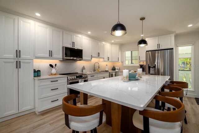1801 Gulf Dr N Unit 276, Bradenton Beach, FL 34217 - kitchen with appliances with stainless steel finishes, light wood-style flooring, a kitchen island, white cabinetry, and tasteful backsplash