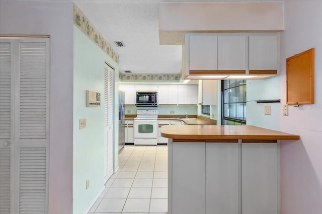 2708 Wilkinson Rd, Sarasota, FL 34231 - kitchen with white range with electric cooktop, black microwave, freestanding refrigerator, a peninsula, and light tile patterned floors