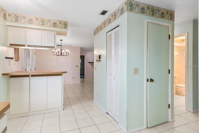 2708 Wilkinson Rd, Sarasota, FL 34231 - kitchen with light tile patterned floors, a textured ceiling, a chandelier, a peninsula, and white cabinets