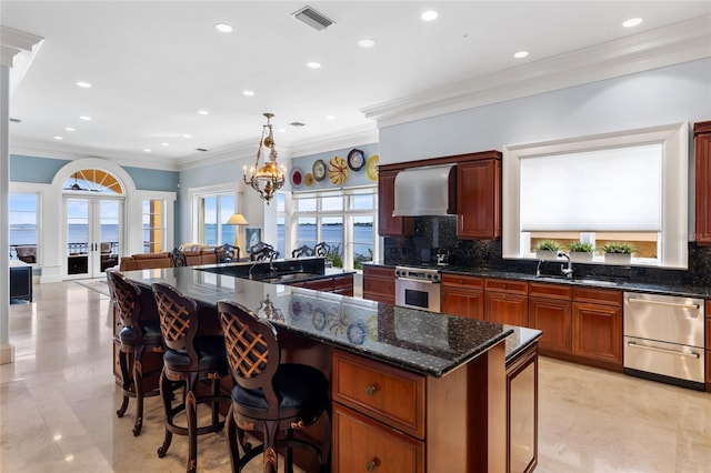 309 Ringling Point Dr, Sarasota, FL 34234 - kitchen with wall chimney exhaust hood, stainless steel appliances, backsplash, crown molding, and dark stone counters