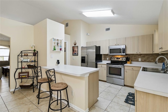 4649 72nd Ct E, Bradenton, FL 34203 - kitchen featuring appliances with stainless steel finishes, a peninsula, vaulted ceiling, light brown cabinets, and a kitchen breakfast bar