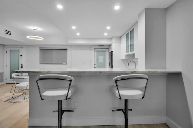 1150 Tarpon Center Dr Unit 1-C # 103, Venice, FL 34285 - kitchen featuring white cabinets, recessed lighting, a kitchen breakfast bar, light stone countertops, and light wood-style flooring