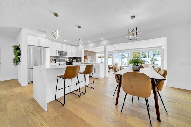 8001 13th Ave S, Saint Petersburg, FL 33707 - kitchen with stainless steel appliances, a kitchen island, light wood finished floors, a breakfast bar area, and white cabinets