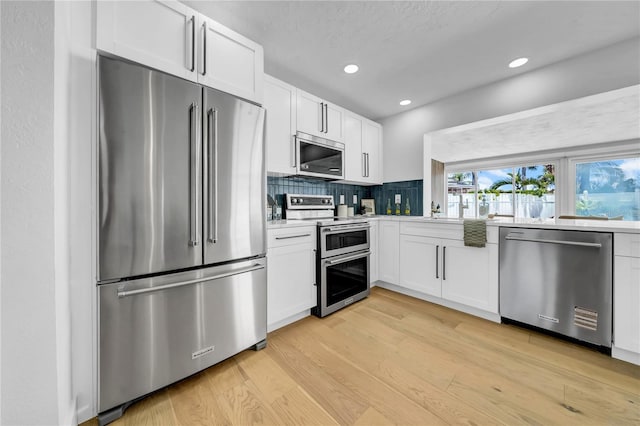 8001 13th Ave S, Saint Petersburg, FL 33707 - kitchen featuring appliances with stainless steel finishes, light wood-style flooring, light countertops, tasteful backsplash, and white cabinetry